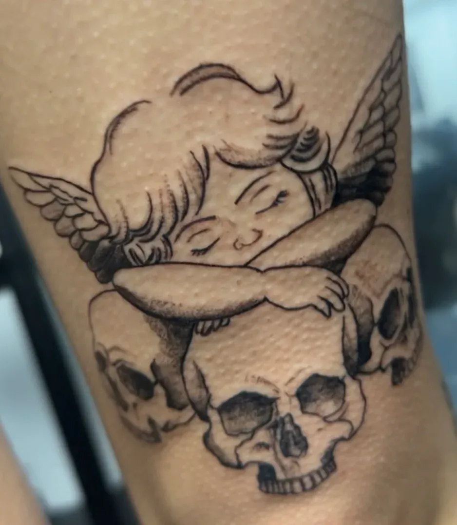 Black and grey cupid over skull tattoo